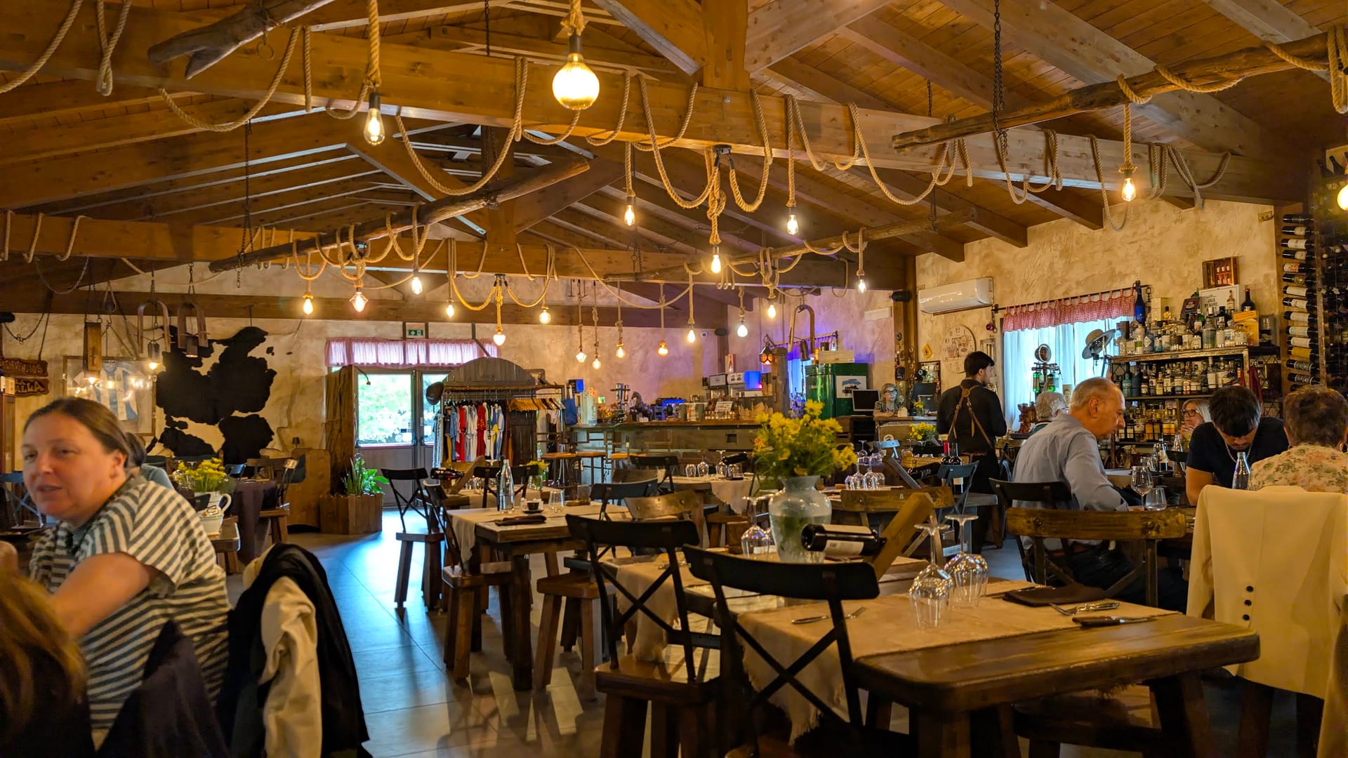 El salón completo de La Stalla de día — vigas de madera, luces Edison y mesas de roble