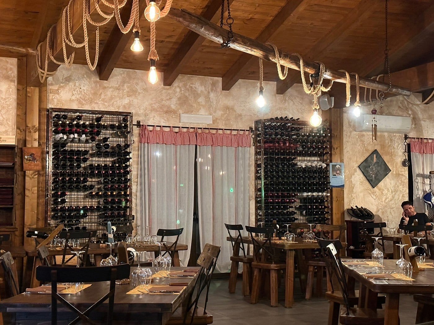 Salón principal de La Stalla — luces Edison, vigas de madera y racks de vino en las paredes